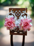 A pair of floral earrings with pink roses and white pearls displayed on a wooden stand against a blurred background.