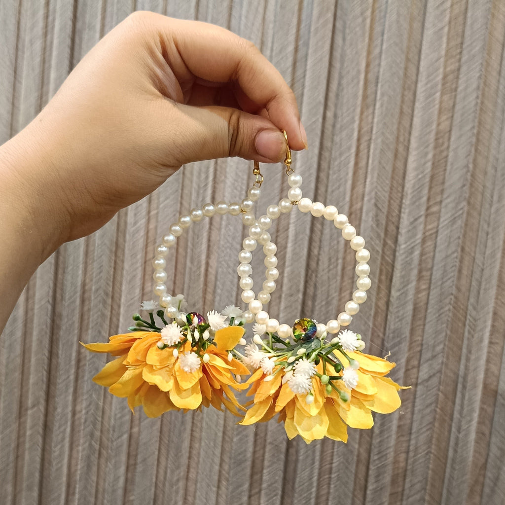 Hand holding a pair of earrings with yellow flowers and pearl-like beads against a wooden background