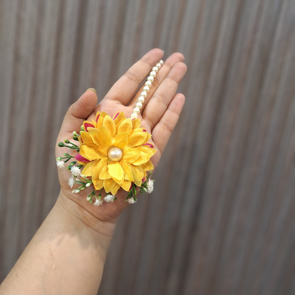 Hand holding a yellow flower with a pearl in the center against a blurred background