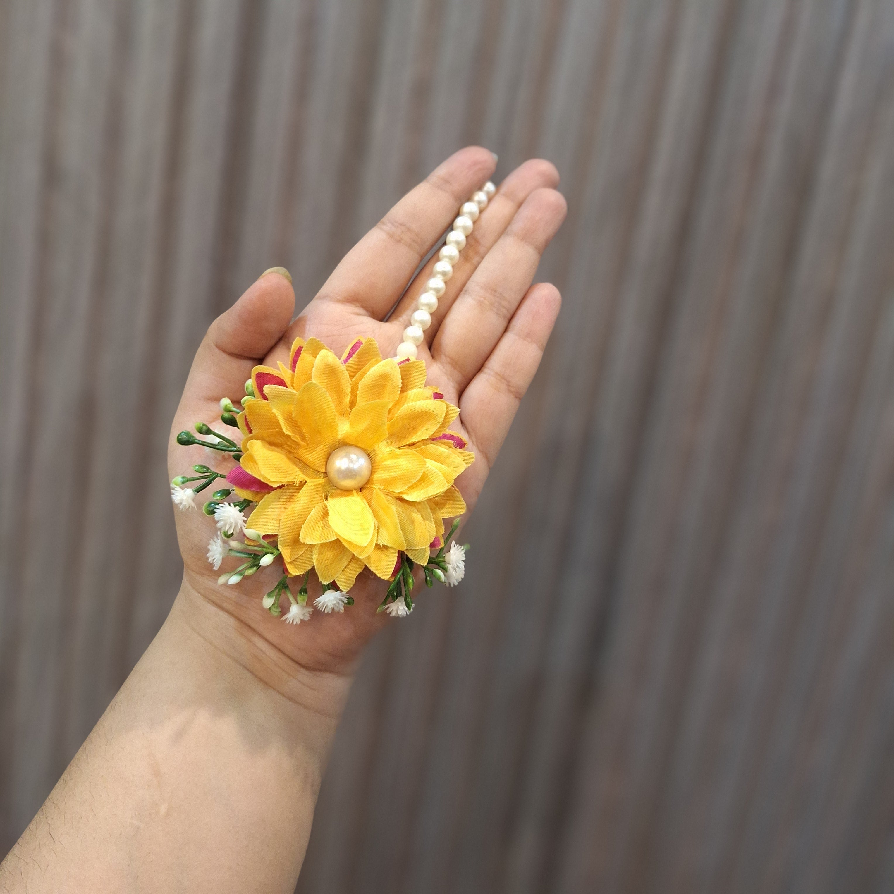 Hand holding a yellow flower with a pearl in the center against a blurred background