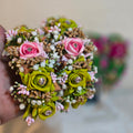 Hand holding a bouquet of artificial flowers with pink and green colors.