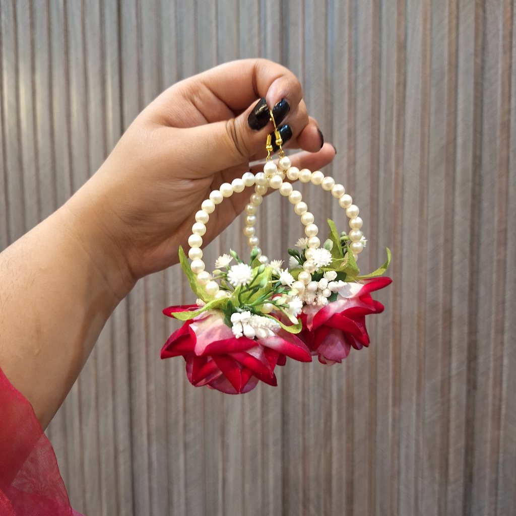 Hand holding a decorative earring with red flowers and pearls against a striped background