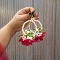 Hand holding a decorative earring with red flowers and pearls against a striped background