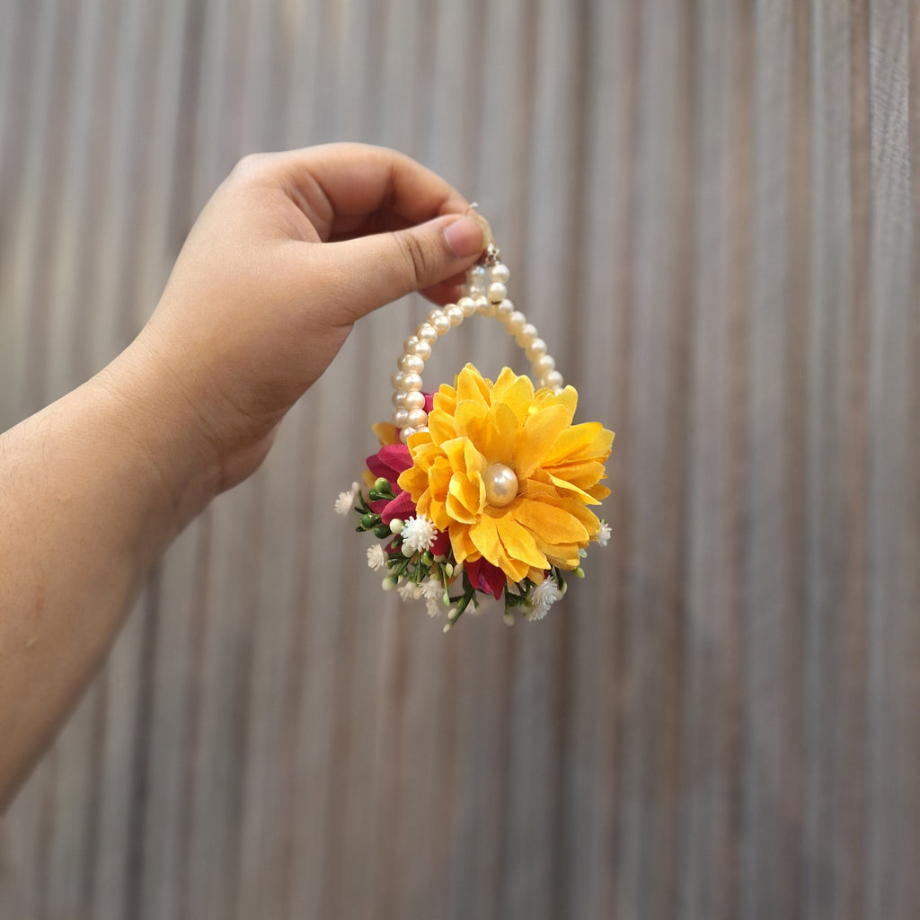 Hand holding a decorative headband with yellow flowers and pearls against a striped background