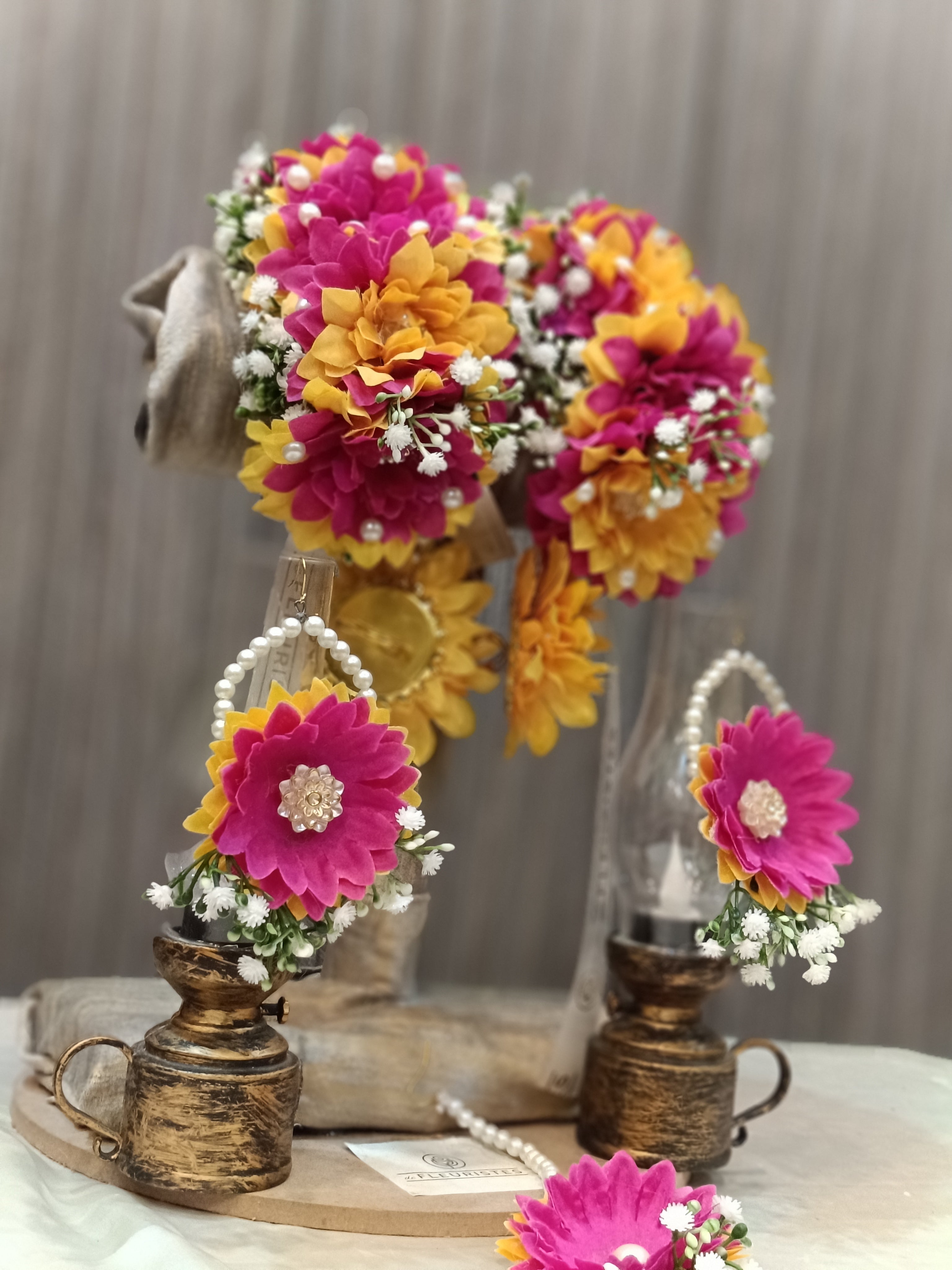 A display of floral jewelry set including a gajra hair accessory, earrings, bindi, and a ring, adorned with artificial chrysanthemum and baby's breath flowers.