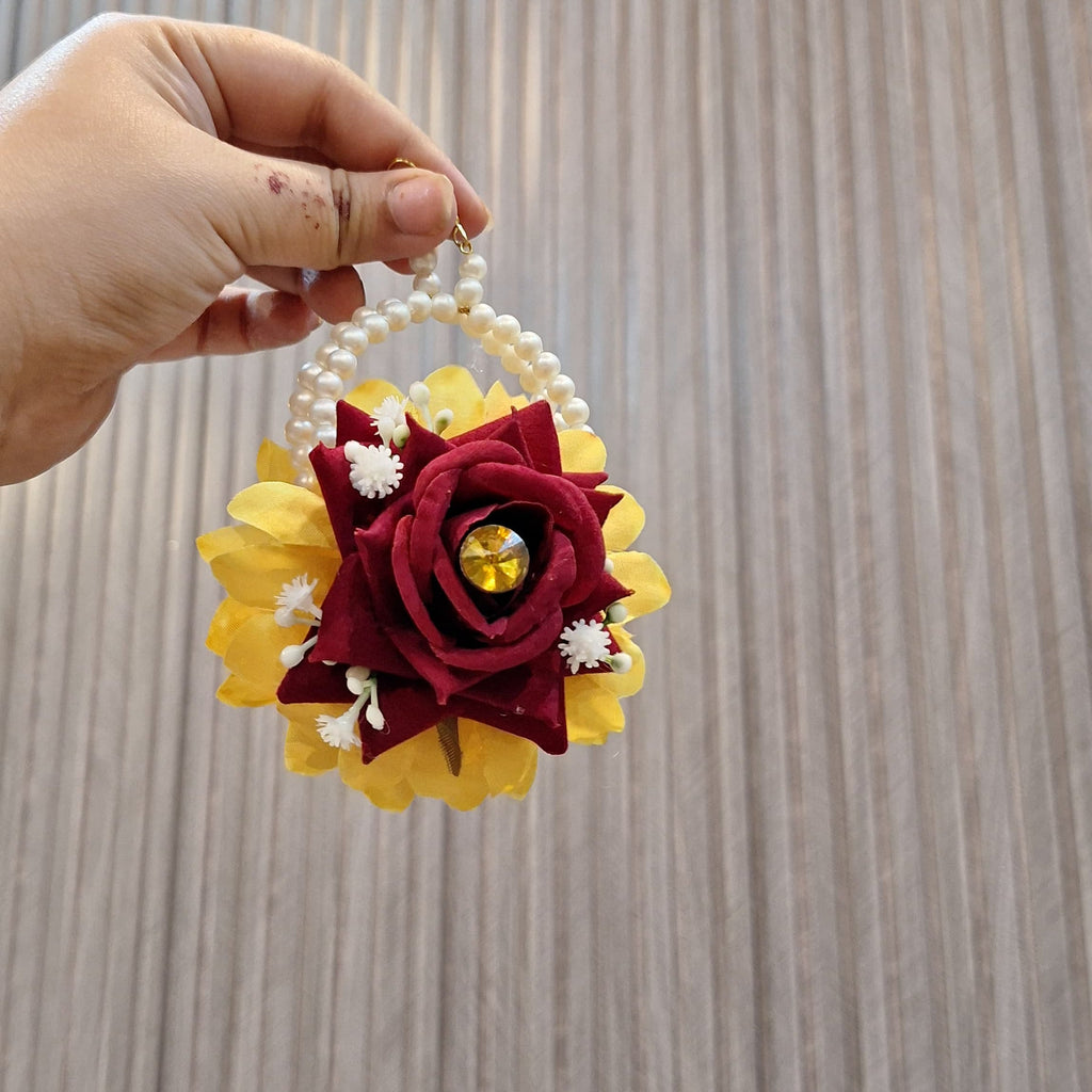 Handmade flower ornament with red and yellow colors held against a neutral background